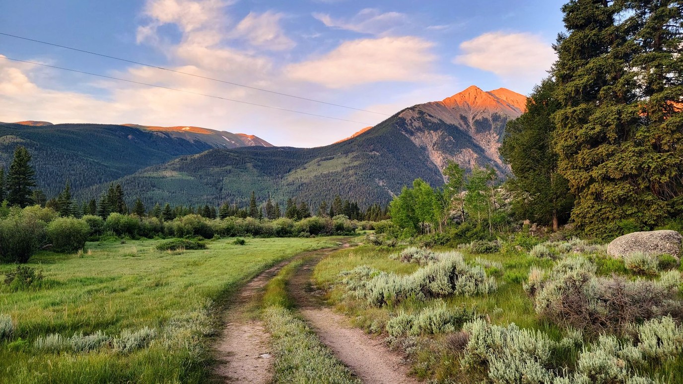 A two track dirt ranch road crossing sagebrush meadow toward a lit peak in the Colorado high country