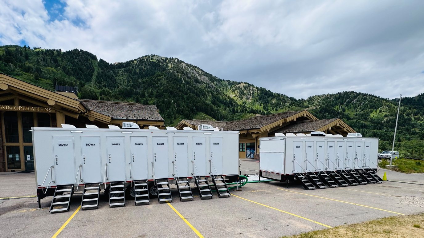 Two eight stall shower trailers side by side on a mountain resort parking lot, a stair and rail at each of the sixteen doors