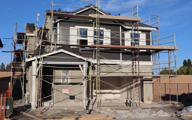 A two story house wrapped in scaffolding partway through an exterior renovation