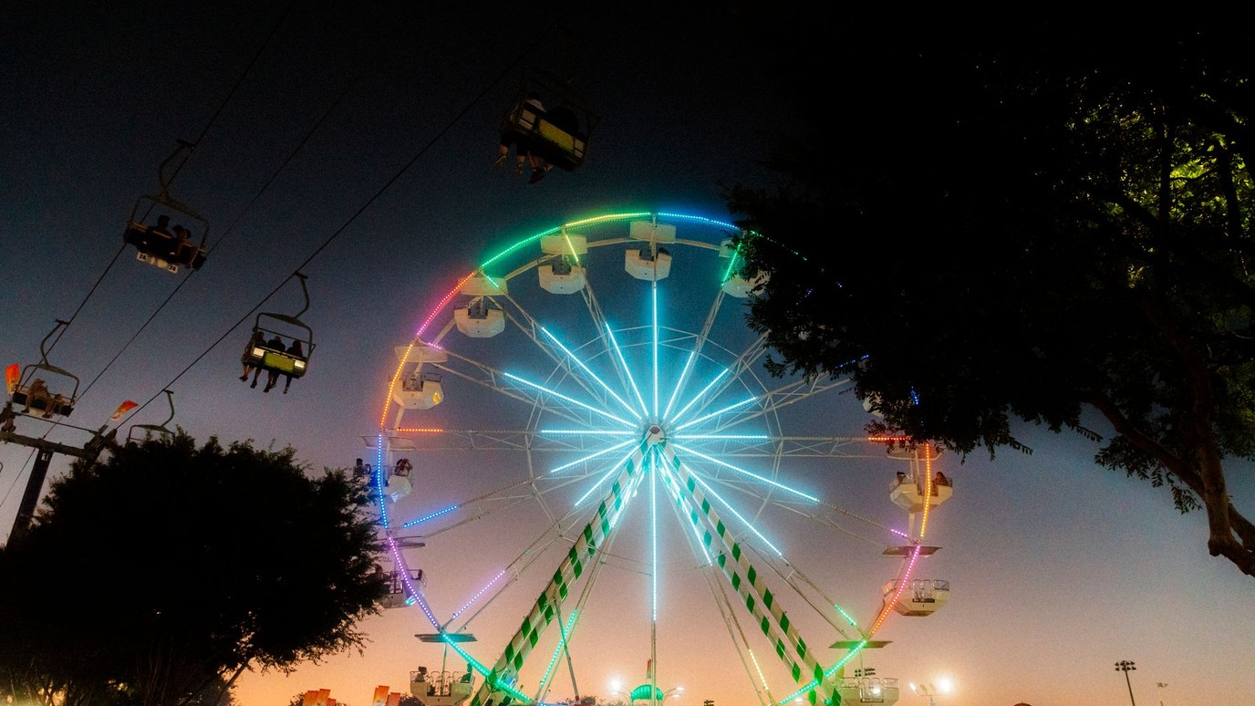 A lit ferris wheel and sky ride over the midway at a county fair at dusk