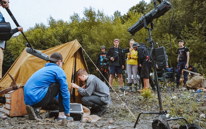 A film crew working a camera, boom and lighting rig on an outdoor forest location