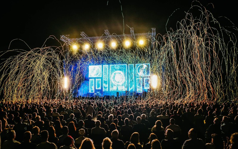 A festival crowd silhouetted against a lit main stage at night