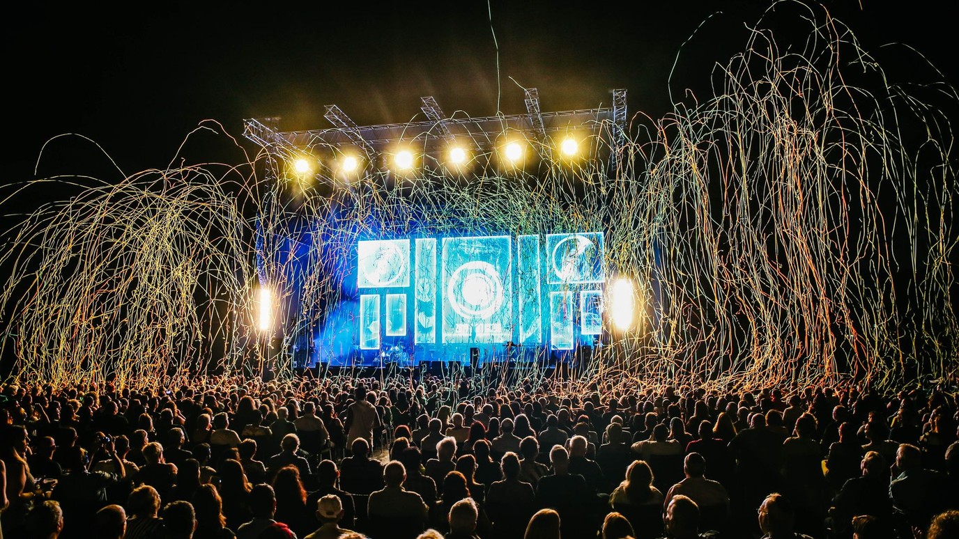 A festival crowd silhouetted against a lit main stage at night