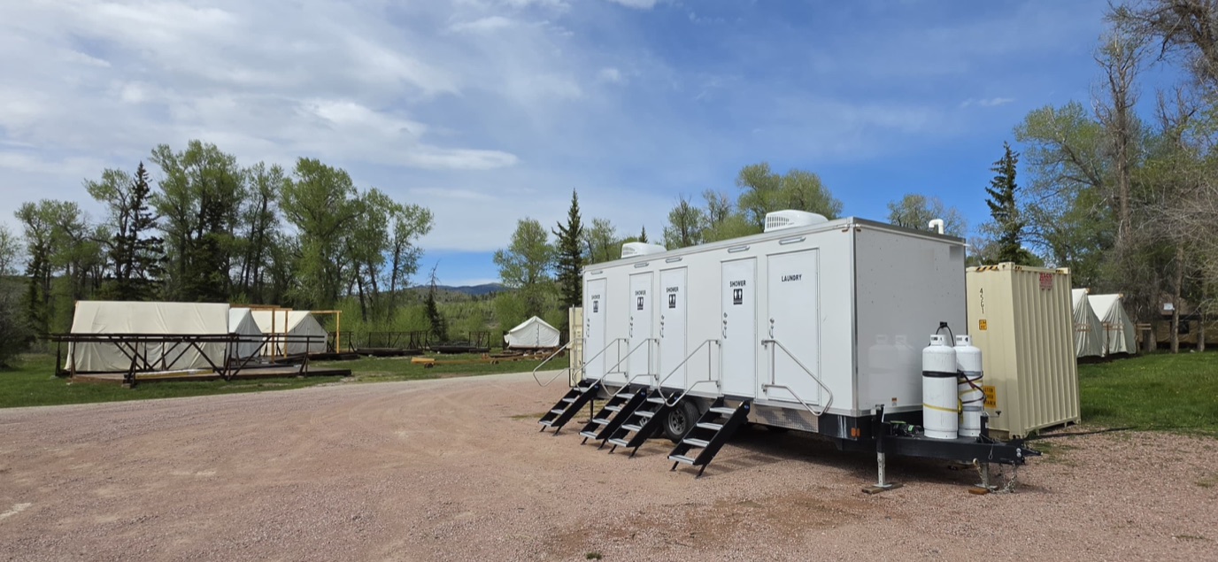 Shower trailer set among canvas wall tents at a remote base camp