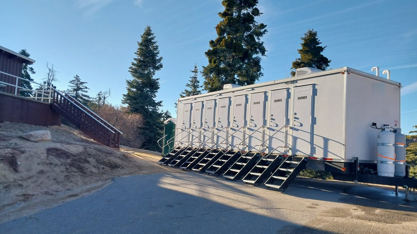 Eight stall shower trailer set on a mountain lodge service lot among tall pines